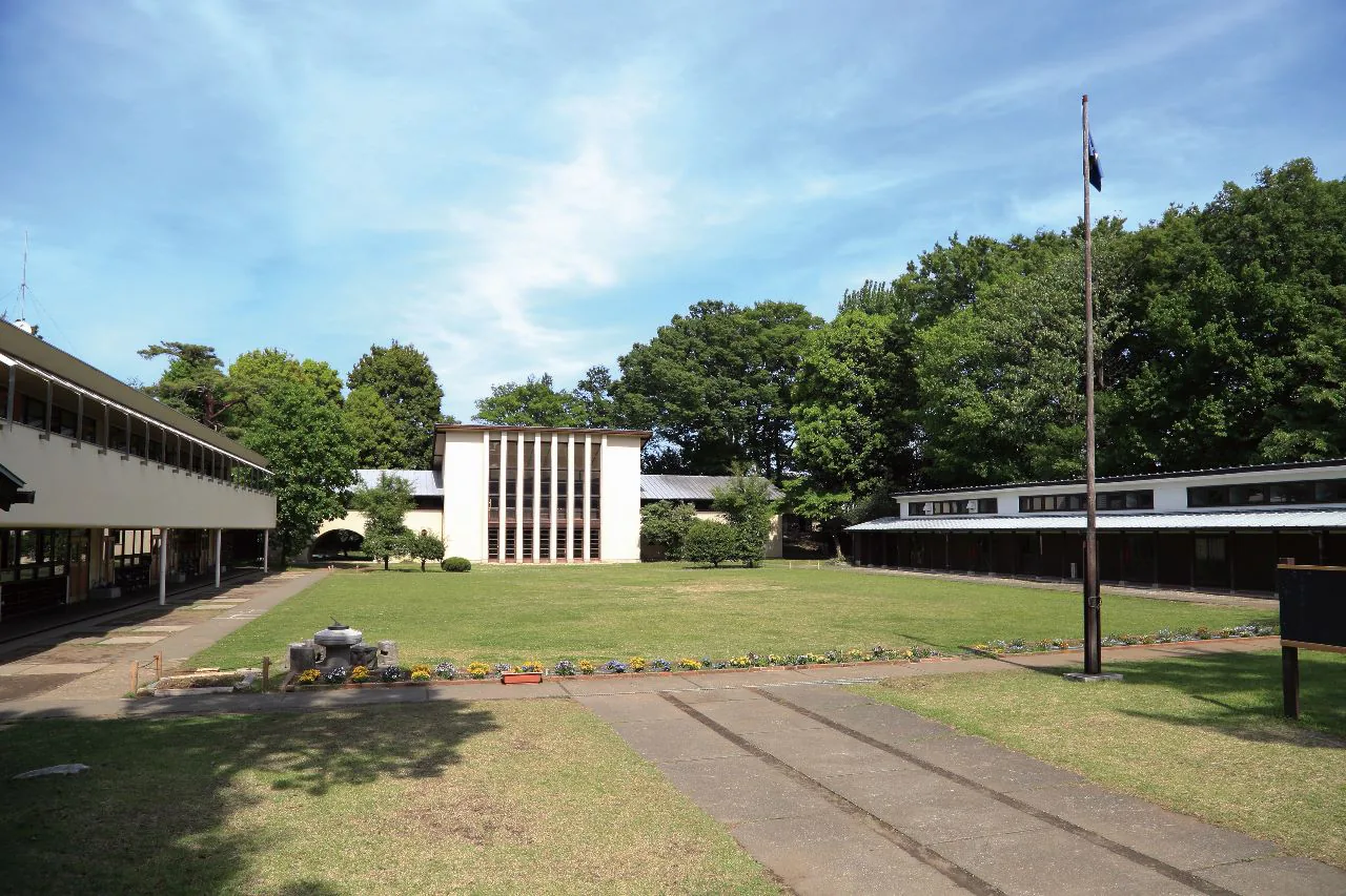 自由学園中等部・高等部の校舎。芝生の広場を囲むように、縦長の窓が並ぶ建物と平屋の校舎が建ち、まわりを木々が囲んでいる