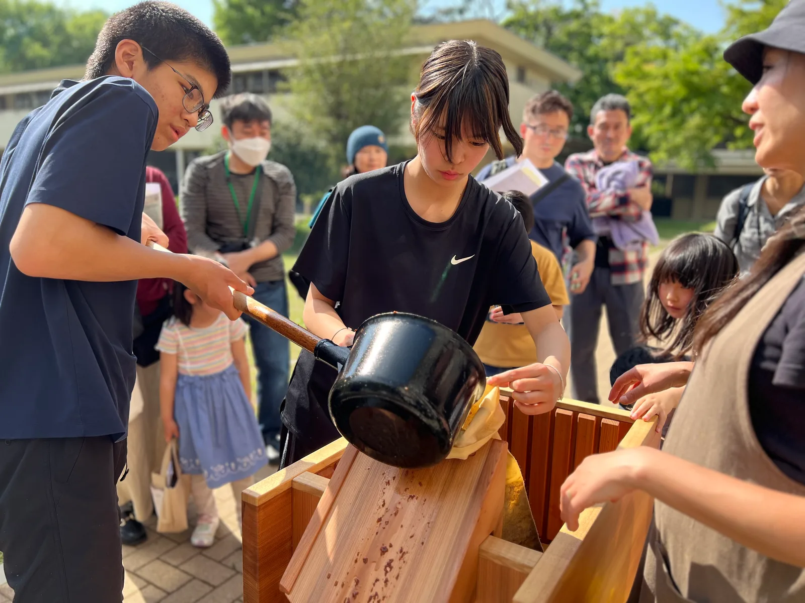 自由学園中等部・高等部の手作り醤油づくりの様子。生徒が鍋から材料を袋に移し、まわりの人が見守っている