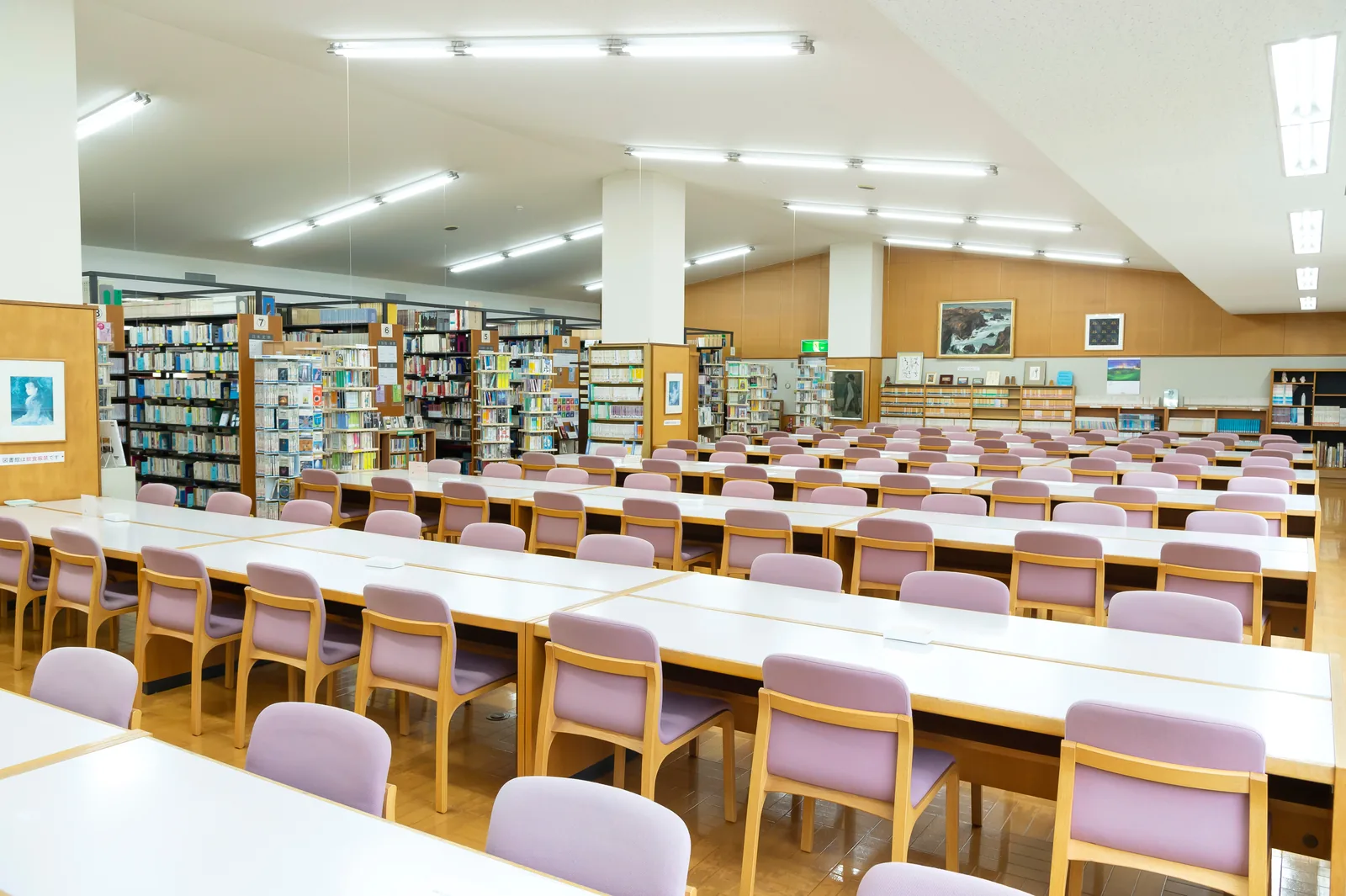 聖園女学院中学校・高等学校の図書館。長机といすが並ぶ閲覧席の奥に、書架と絵画が見える