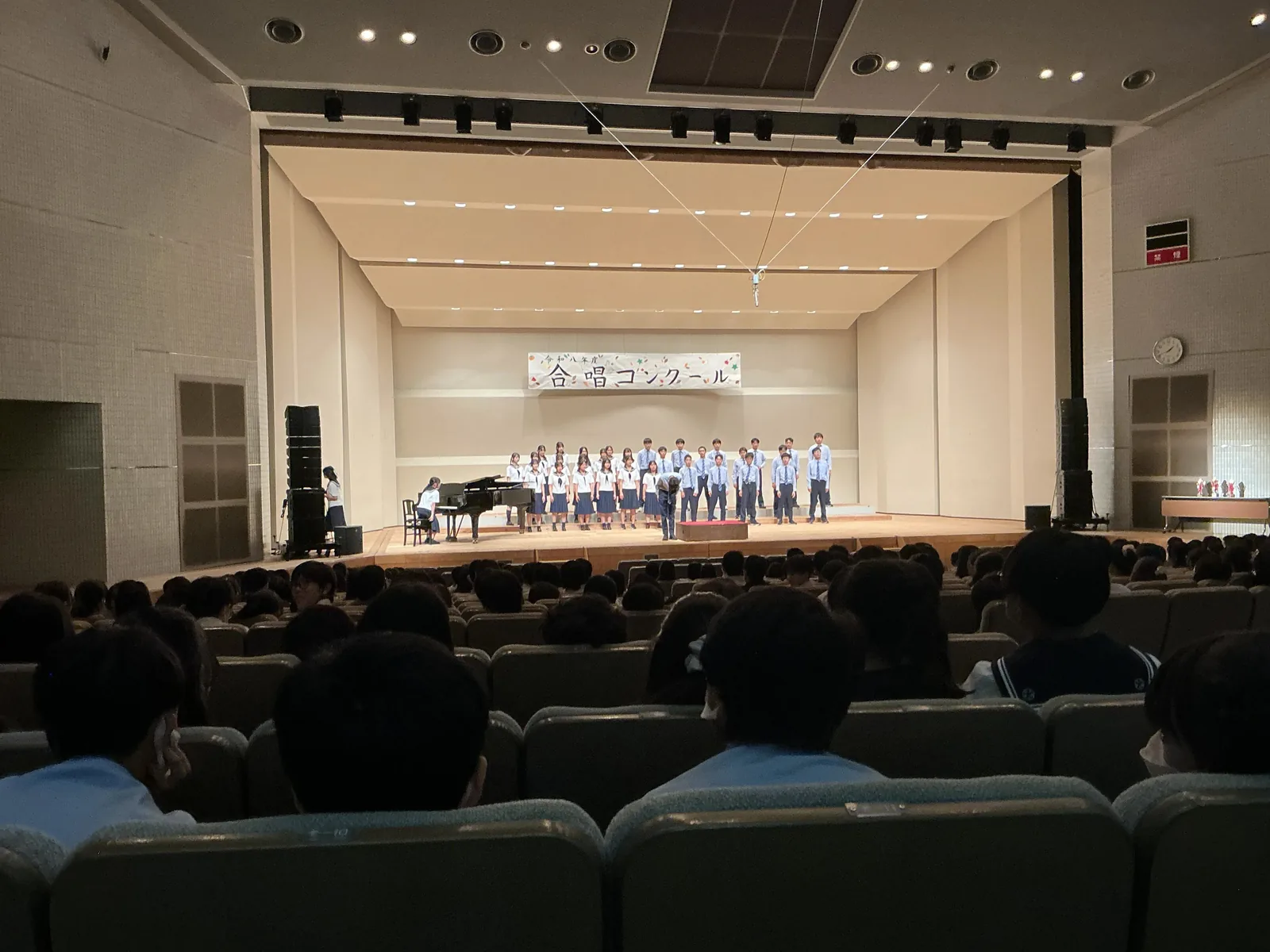 昭和学院秀英中学校・高等学校の合唱コンクール。ホールの舞台に並んだ生徒たちを、客席の生徒が見ている