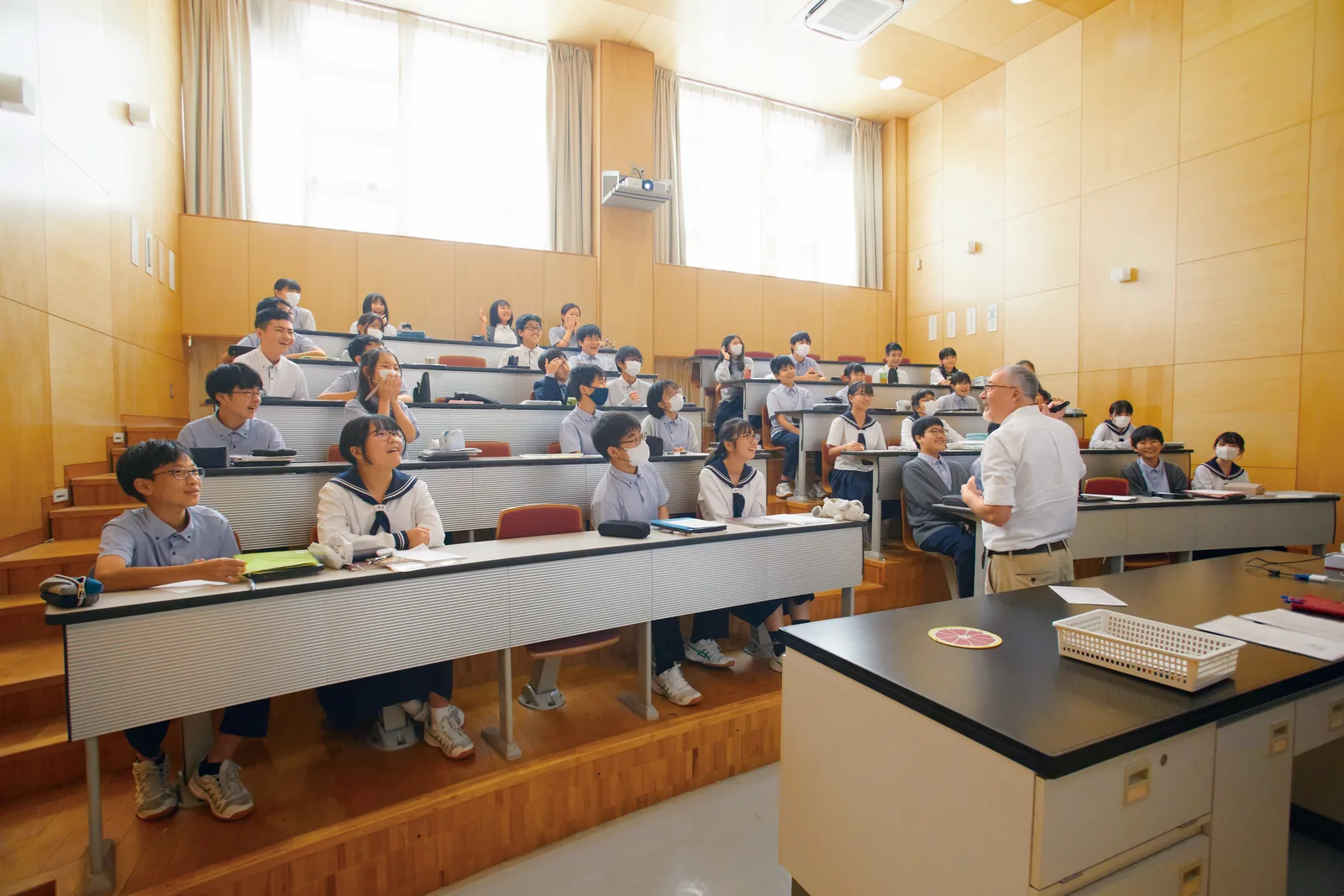 昭和学院秀英中学校・高等学校の階段教室。段状に並んだ席の生徒たちが、前に立つ先生の話を笑顔で聞いている