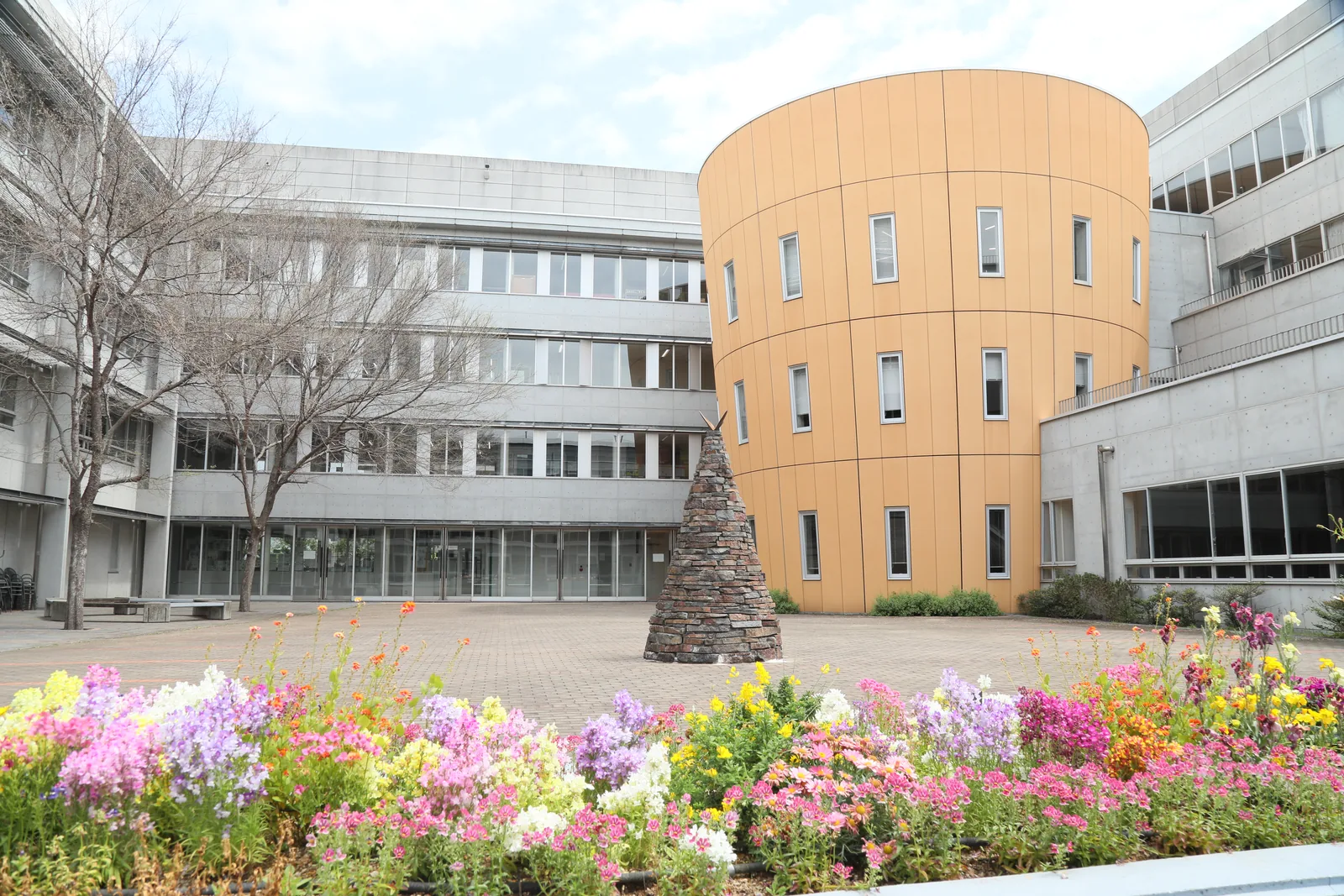 東京都市大学付属中学校・高等学校の中庭。花壇に花が咲き、円筒形の校舎が建っている