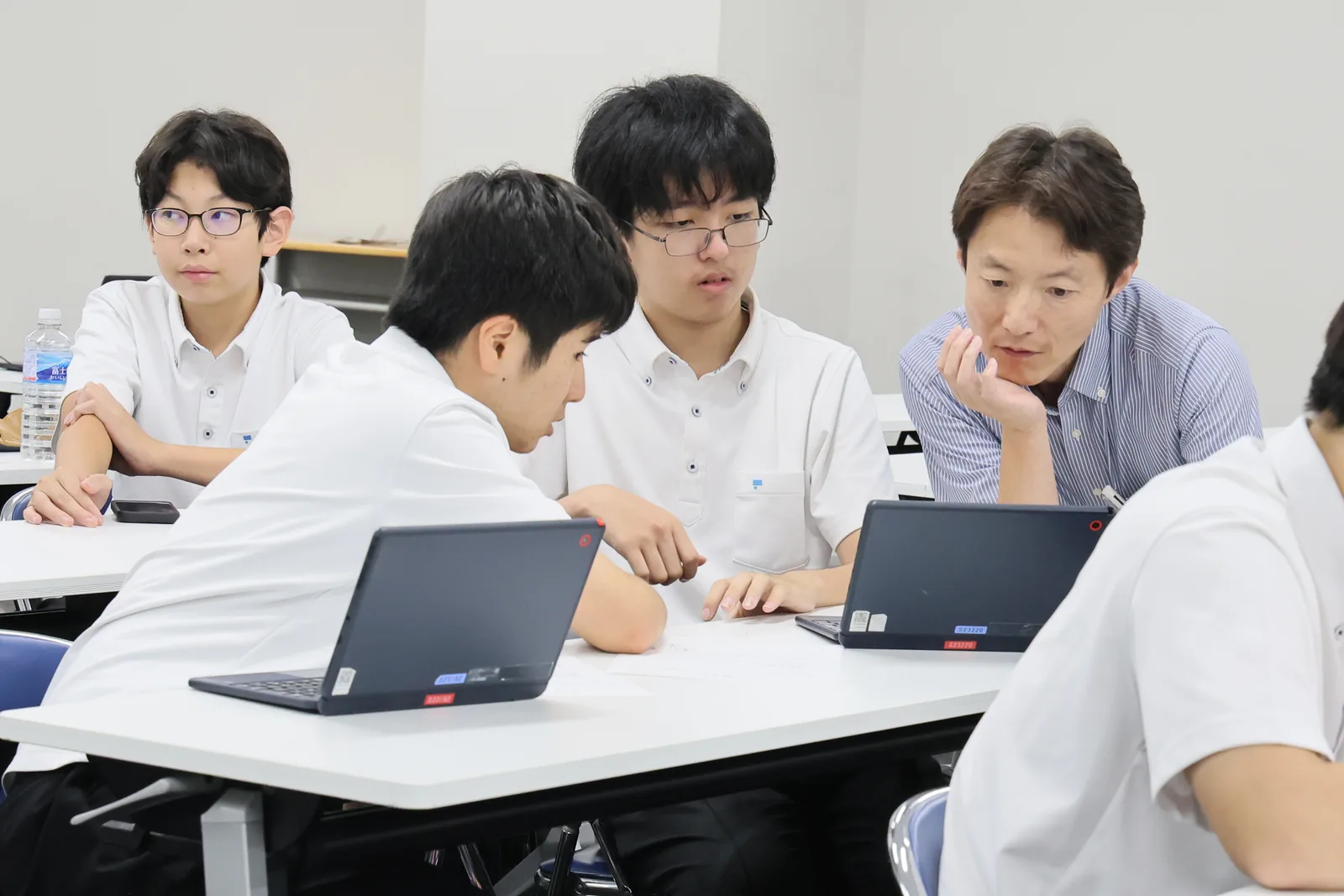 東京都市大学付属中学校・高等学校の教室での学習の様子。ノートパソコンを広げた生徒たちの輪に教員が加わり、一緒に画面を見ている