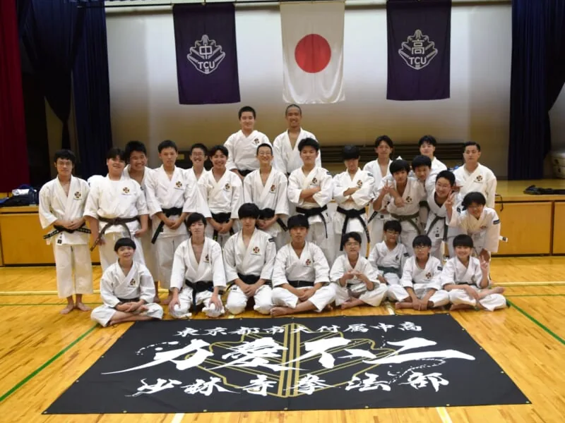 東京都市大学付属中学校・高等学校の少林寺拳法部。道着姿の部員が部旗を囲んで並んでいる