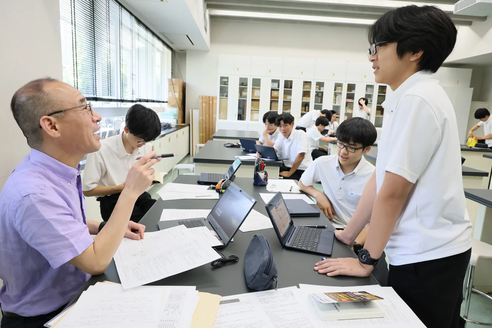 東京都市大学付属中学校・高等学校の中期修論アドバイスデー。教員が机の上の原稿を前に、生徒と話している